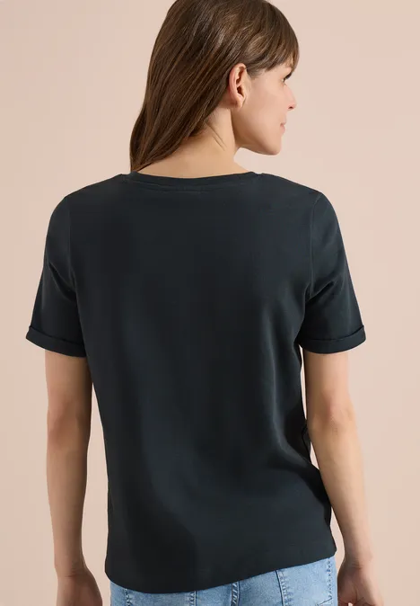 Femme vue de dos portant un t-shirt noir simple sur fond beige