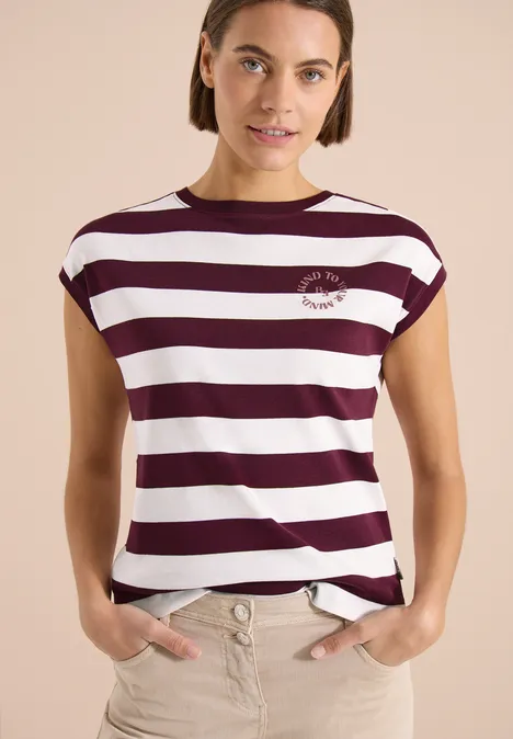 Vrouw draagt wit-paars gestreept shirt voor een effen achtergrond.