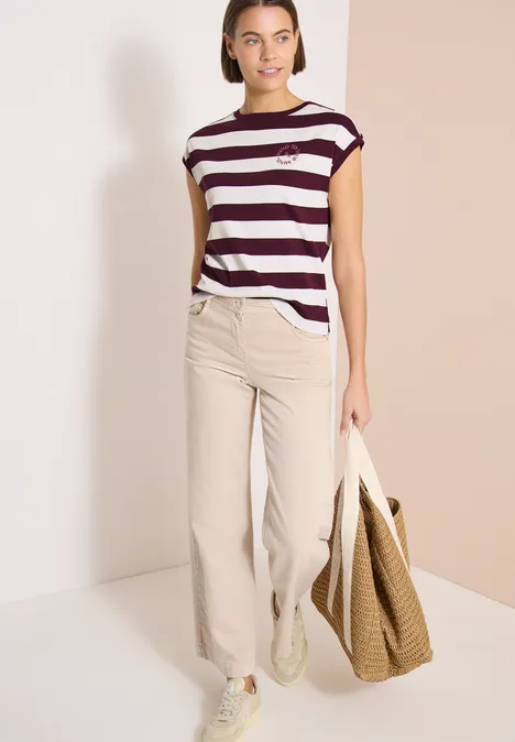 Vrouw in gestreept T-shirt en beige broek met grote, grofgebreide tas