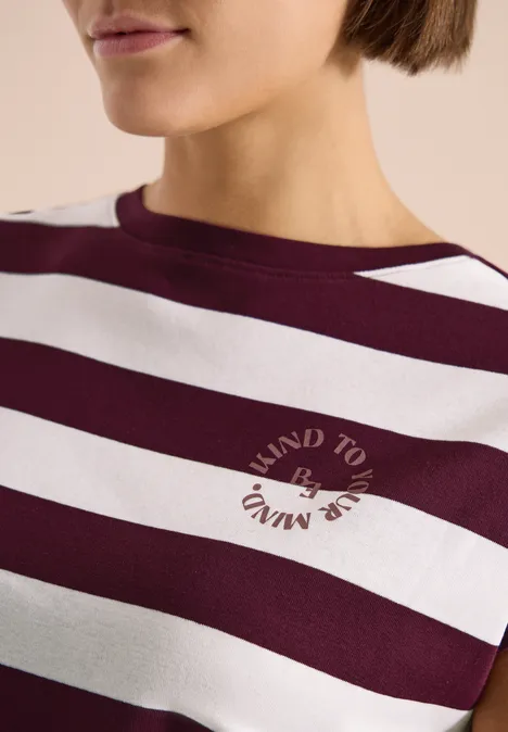 Close-up van een vrouw in een bordeaux-wit gestreept shirt met ronde tekst op de borst.