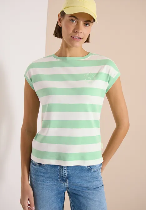 Vrouw in groen-wit gestreept T-shirt en spijkerbroek voor lichte achtergrond.