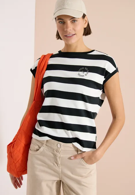 Model met zwart-wit gestreept T-shirt, beige broek, oranje tas en pet.