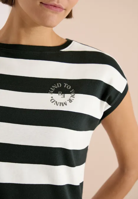 Een vrouw draagt een kort T-shirt met brede zwart-witte strepen en een rond logo op de borst.