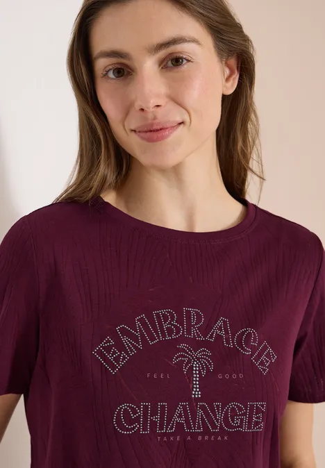 Frau in bordeauxrotem T-Shirt mit Aufschrift 'Embrace Change' und Palmenmotiv.