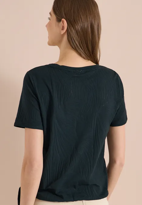 Frau steht mit dem Rücken zur Kamera und trägt ein schlichtes schwarzes T-Shirt.