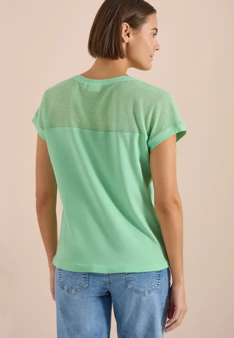 Vrouw van achteren in mintgroen T-shirt en blauwe spijkerbroek voor beige achtergrond.
