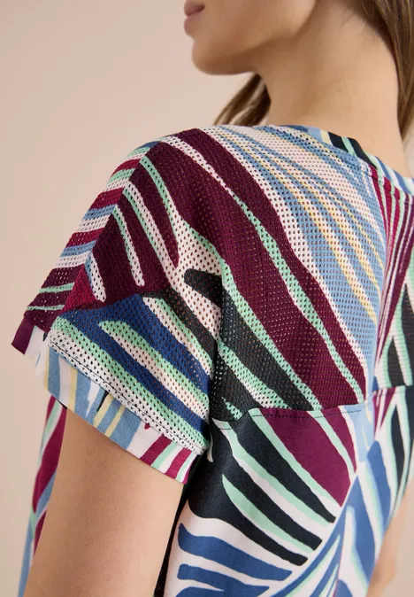 Frau im Profil mit bunt gestreiftem, kurzärmligem Stricktop.