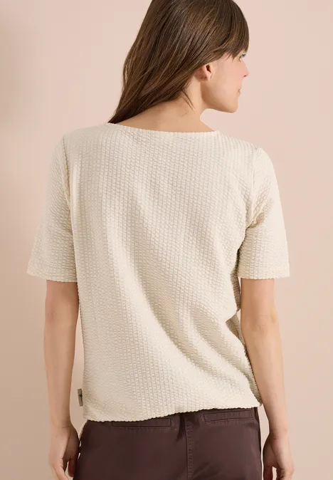 Achteraanzicht van een vrouw in een beige wafelstof-T-shirt met korte mouwen voor een lichte achtergrond.