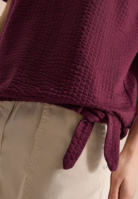 Donkerpaarse gewatteerde top met zijstrik, gecombineerd met beige broek.