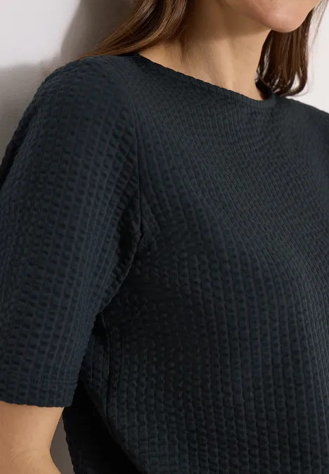 Frau trägt schwarzes, kurzärmeliges, gewaffeltes Oberteil mit Rundhalsausschnitt.