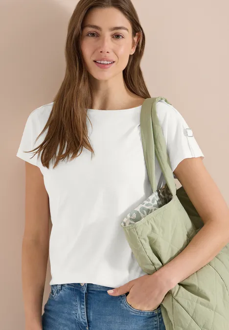 Vrouw draagt een wit t-shirt, blauwe jeans en een groene doorgestikte schoudertas.