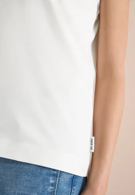 Wit mouwloos topje van licht materiaal, valt los over blauwe jeans, met klein zijlabel.