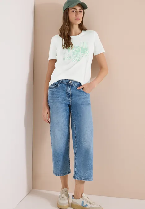Frau in weißem T-Shirt und weiten Jeans-Culotte, lässiger Alltagslook mit Sneakers.