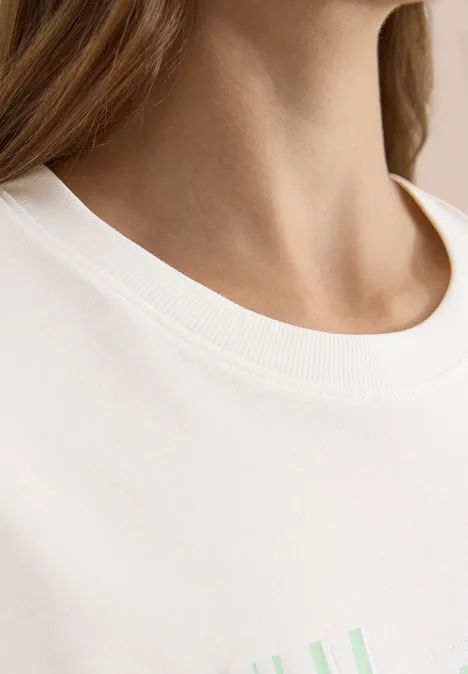 Nahaufnahme von Hals und weißem T-Shirt mit pastellgrünem Aufdruck.