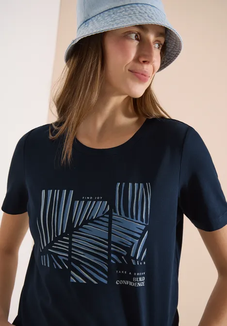 Model trägt dunkles T-Shirt mit abstraktem Streifendesign und einen hellen Eimerhut.