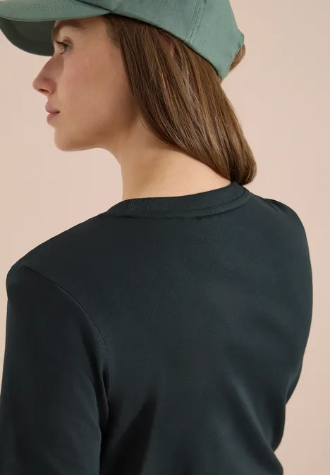 Achteraanzicht van een persoon met een donker groen T-shirt en een lichtgroene pet voor een beige achtergrond.