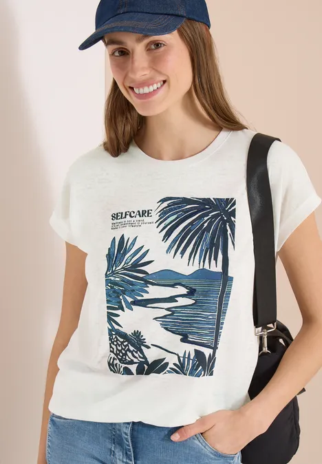 Persoon draagt een wit t-shirt met palmprint, blauwe pet en zwarte schoudertas.
