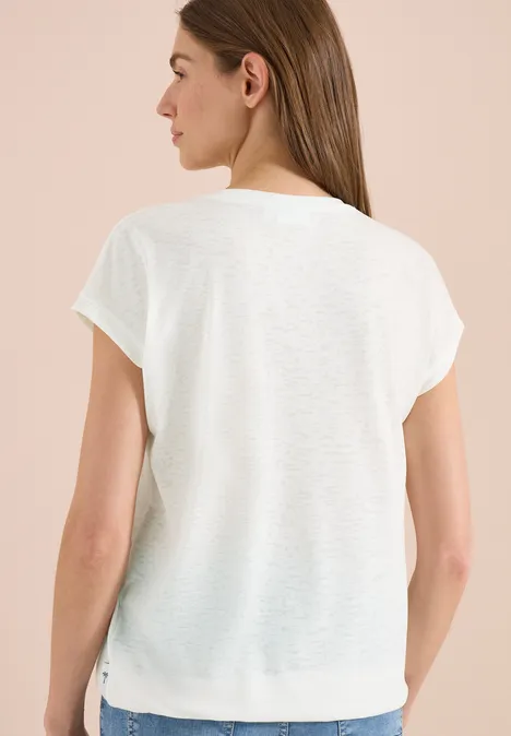 Achteraanzicht van een vrouw in een wijd, wit T-shirt met korte mouwen tegen een neutrale achtergrond.