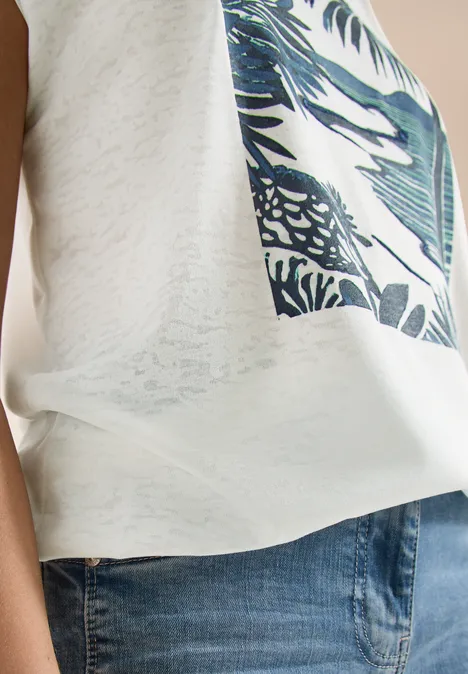 Zijaanzicht van iemand met een wit T-shirt met tropische print en een blauwe spijkerbroek.