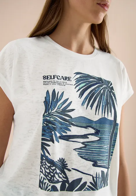 Vrouw draagt een wit T-shirt met blauwe tropische print en opschrift 'SELFCARE'.