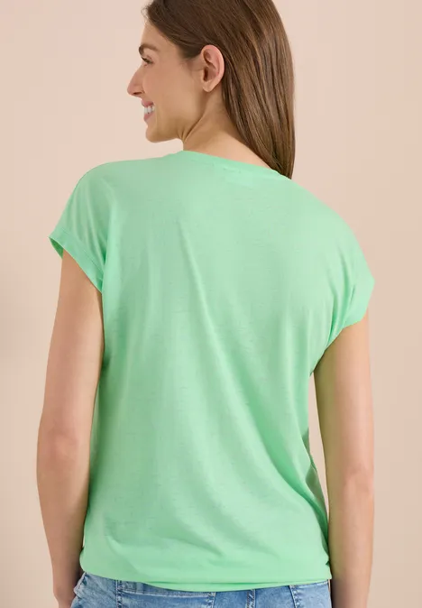 Vrouw van achteren met mintgroen T-shirt en korte mouwen tegen een neutrale achtergrond.