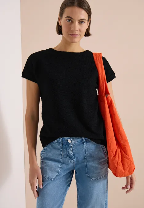 T-Shirt mit Boatneck im Ajour-Look Black Eine Person trägt ein schwarzes T-Shirt, blaue Jeans und eine orangefarbene gesteppte Umhängetasche.
