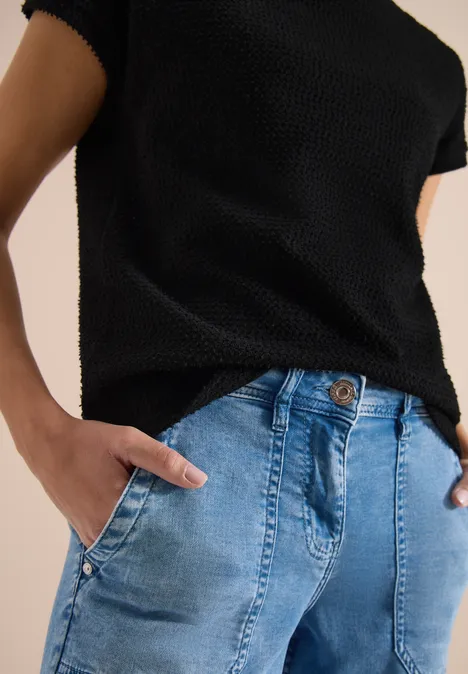 T-Shirt mit Boatneck im Ajour-Look Black Schwarzes Strickshirt, hellblaue Jeans, Hände in den Taschen.