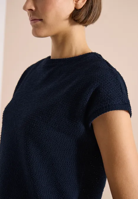 T-Shirt mit Boatneck im Ajour-Look universal blue Dunkelblaues, strukturiertes Strickshirt mit kurzen Ärmeln an einer Frau vor beigem Hintergrund.