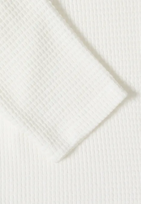 Close-up van wit geweven stof met wafeltjesstructuur, ruitpatroon.