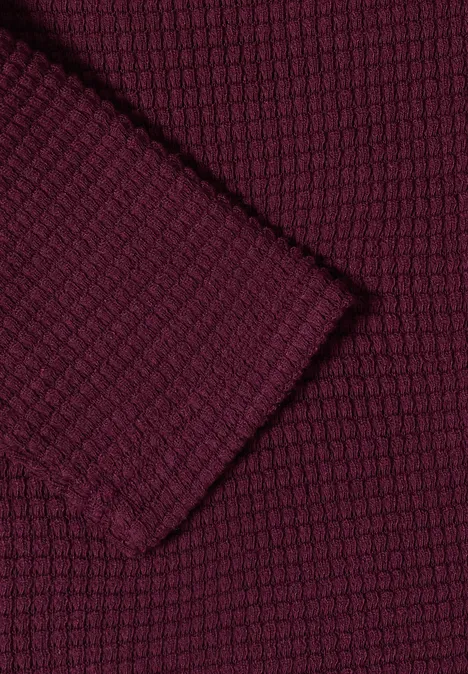 Close-up van een bordeauxrode gebreide stof met gestructureerd wafelpatroon.