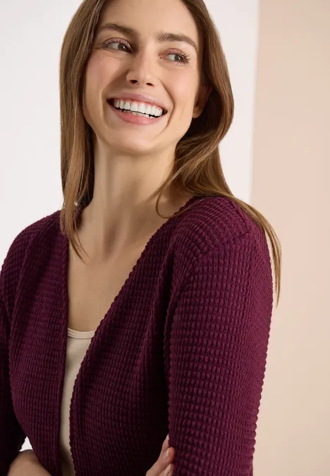 Vrouw met paarse gebreide jas over een wit topje voor een neutrale achtergrond