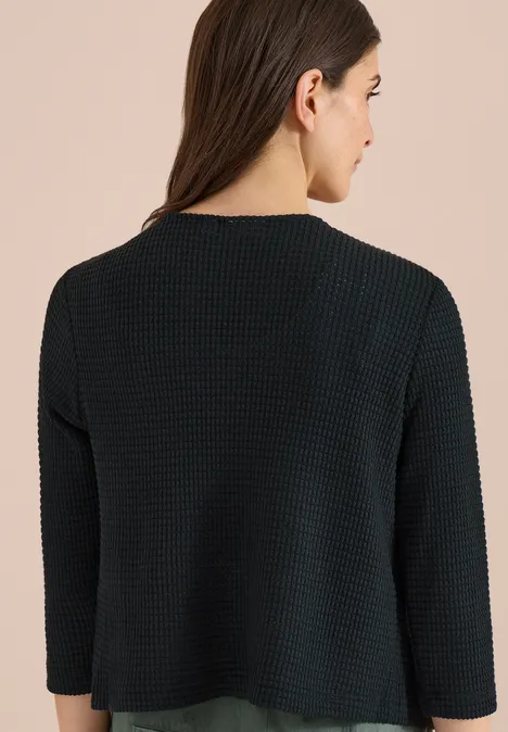 Vrouw van achteren in zwart, textuurgebreid shirt met driekwartmouwen.