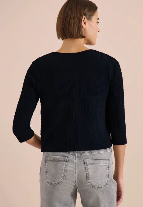 Offene 3/4-Arm Jacke im Ajour-Look universal blue Frau von hinten in schwarzem 3/4-Arm-Shirt und hellgrauer Jeans vor neutralem Hintergrund.