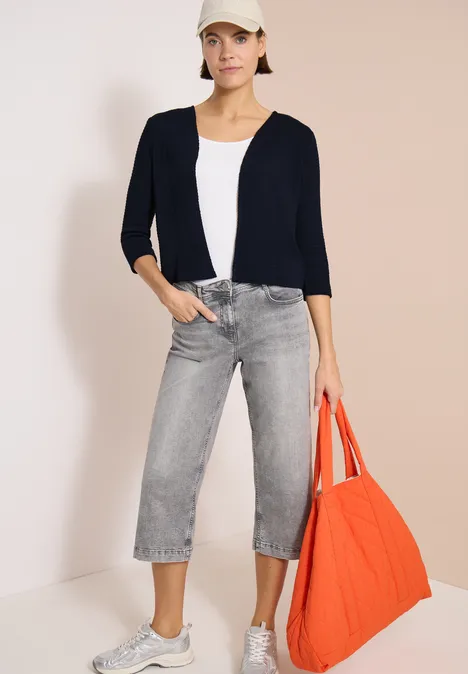 Offene 3/4-Arm Jacke im Ajour-Look universal blue Frau trägt dunkelblauen Cardigan, weißes Top, graue Culotte-Jeans und hält eine große orange Stofftasche.