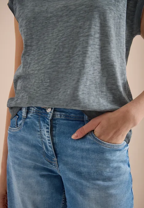Person trägt graues T-Shirt und blaue Jeans, eine Hand in Jeans-Tasche.