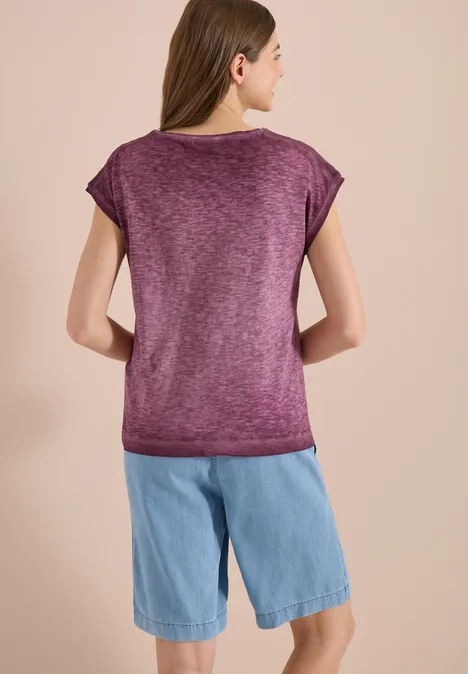 Eine Frau von hinten, die ein lila T-Shirt und blaue Jeans-Shorts trägt.