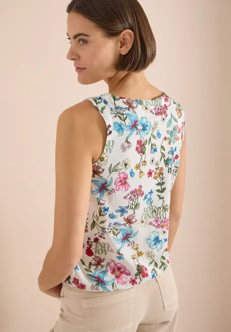 Vrouw van achteren in een witte mouwloze top met kleurrijke bloemenprint en lichte broek.