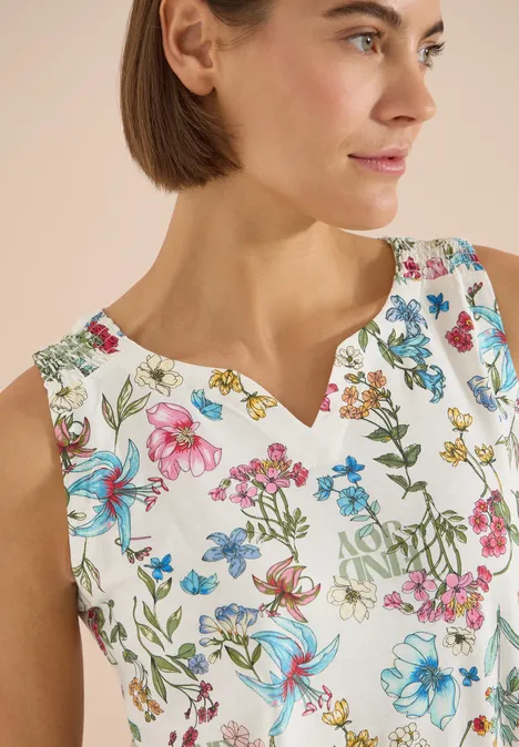 Vrouw in een mouwloze witte top met kleurrijke bloemenprint en V-hals