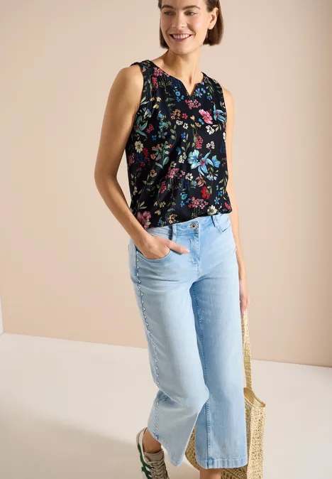 Top mit Split Neck und Raffung universal blue Frau trägt ärmelloses schwarzes Top mit buntem Blumenmuster und hellblaue, weite Jeans mit Saumschlitzen.