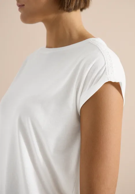 T-Shirt mit Crochet-Details vanilla white Nahaufnahme einer Frau, die ein weißes, kurzärmeliges Oberteil mit feiner Schulternaht trägt.