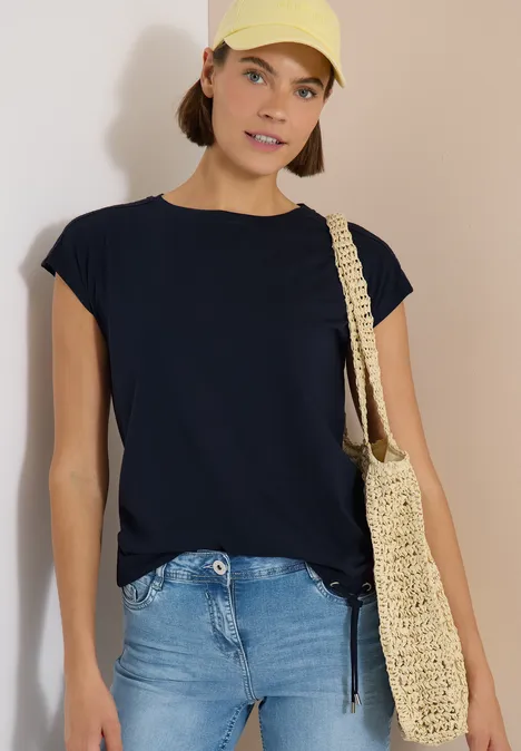 Eine Person trägt ein schwarzes T-Shirt, blaue Jeans und eine gehäkelte Tasche.