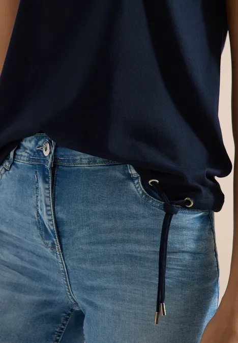 Nahaufnahme: Person trägt blaue Jeans mit Kordelzug an der Taille und dunkelblaues Oberteil.