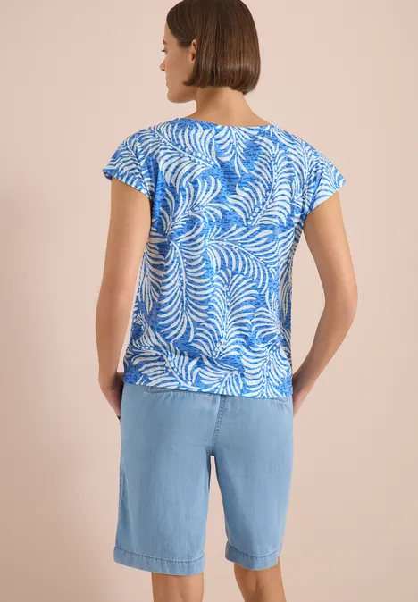 T-shirt à l'effet dévoré null Frau von hinten in blau-weiß gemustertem Shirt und hellblauen Denim-Bermudas vor beigem Hintergrund.