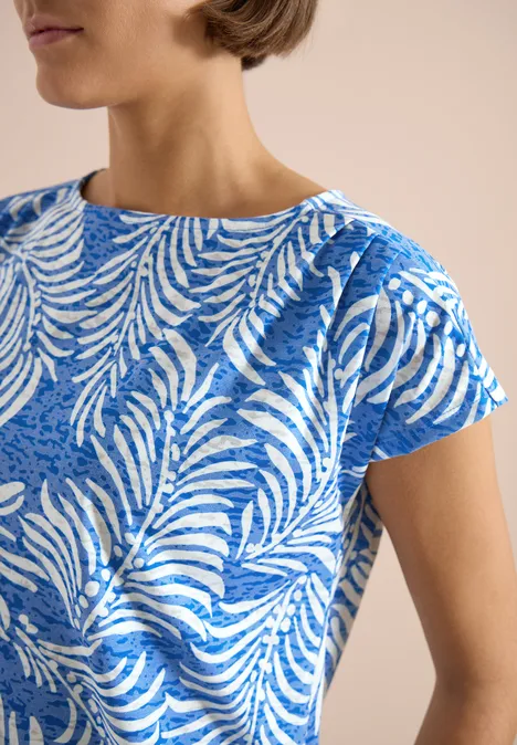 T-shirt à l'effet dévoré null Nahaufnahme eines blauen Kurzarmshirts mit weißem Blattmuster am Oberkörper einer Person.