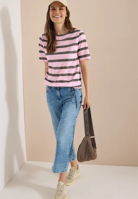 T-Shirt in Ausbrenner-Optik raw khaki Frau trägt rosa-weiß gestreiftes T-Shirt, blaue Jeans, helle Sneakers und hält eine braune Tasche.