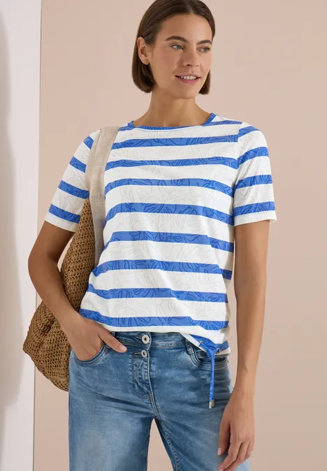 Shirt met burn-out look surf blue Vrouw draagt blauw-wit gestreept shirt, blauwe jeans en een strotas over de schouder.