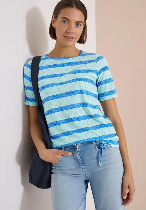 Shirt met burn-out look null Vrouw in lichtblauw-wit gestreept t-shirt met knoop, spijkerbroek en donkere blauwe schoudertas.