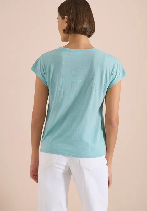 Frau von hinten in hellblauem T-Shirt und weißer Hose.
