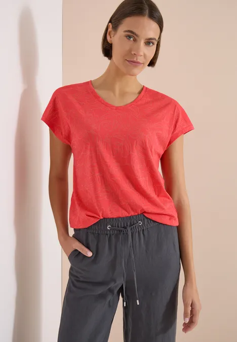 Frau in pinkem T-Shirt und grauen Jogginghosen vor hellem Hintergrund.