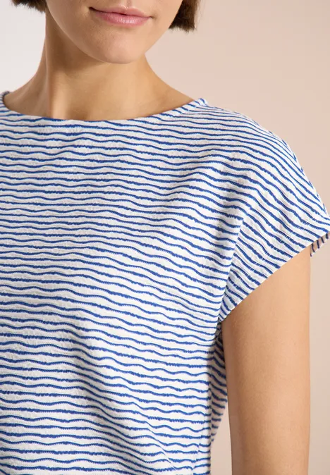 Oberkörper einer Person im weißen T-Shirt mit feinen blauen Streifen und kurzen Ärmeln.